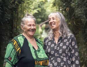 Deux femmes aux cheveux gris, souriantes et complices, posent côte à côte au cœur d'une végétation luxuriante de bambous.