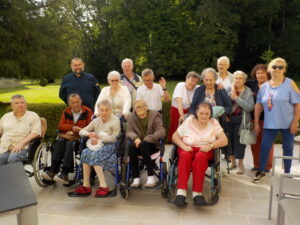 Groupe de personnes âgées, certaines en fauteuil roulant, posant ensemble à l’extérieur avec leurs accompagnants.