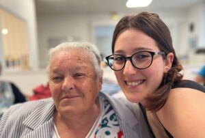 Une femme âgée et une jeune femme souriante posent côte à côte dans un lieu de vie collectif.