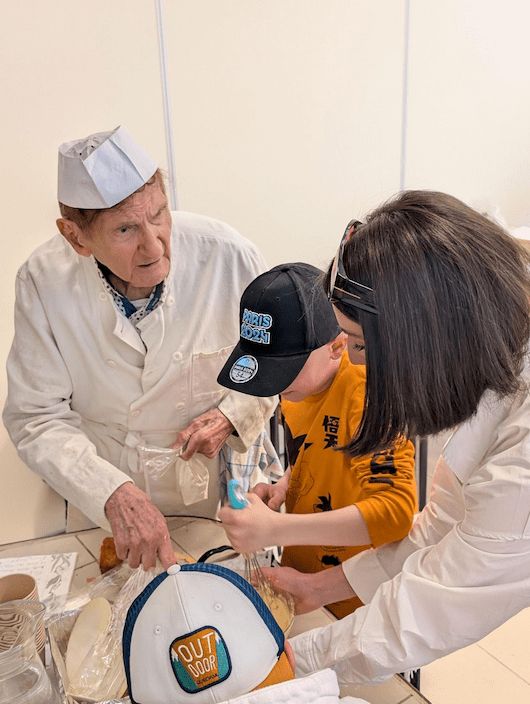 Photo d'une personne accompagnée montrant des techniques de patisserie à un écolier de CM1 pendant la journée intergénérationnelle européenne de 2025 dans la maison d'accueil du Manier des Petits Frères des Pauvres à Marseille
