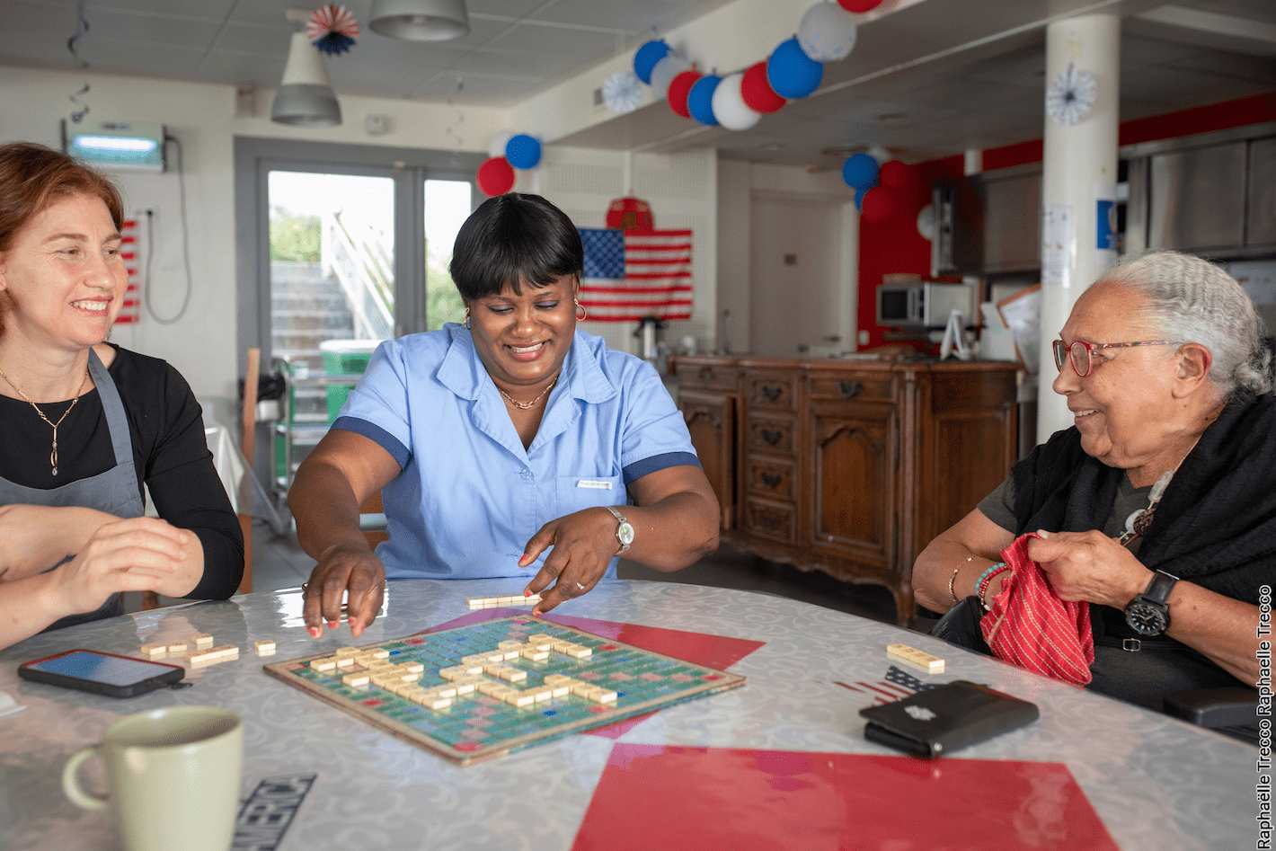 Trois femmes riant dans une pension de famille des Petits Frères des Pauvres devant un plateau de Scrabble