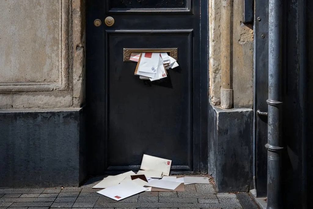 Une porte noire avec une accumulation de lettres non relevées, certaines tombées au sol.