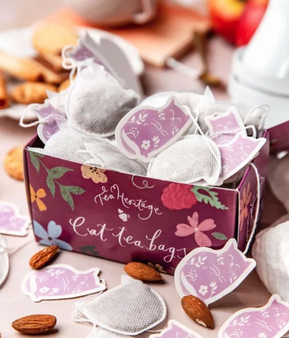 Boîte de sachets de thé en forme de chat, avec des infusettes et des amandes autour.