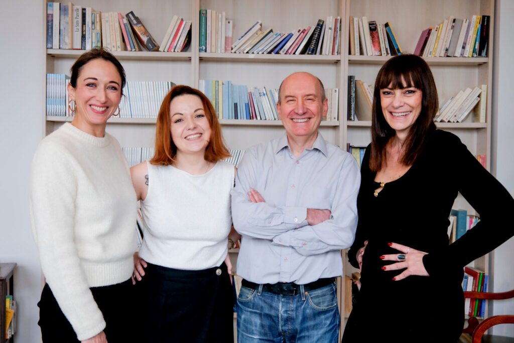 Quatre personnes souriantes posant ensemble devant une bibliothèque remplie de livres.