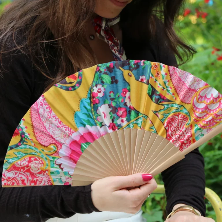 Femme tenant un éventail coloré à motifs floraux et oiseaux, avec une structure en bois.