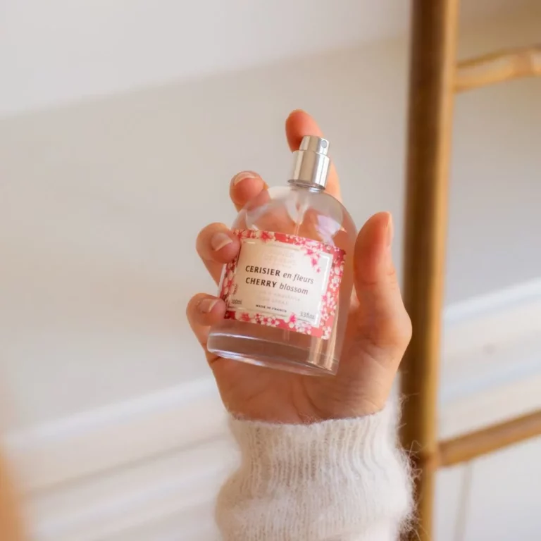 Main tenant un spray d’ambiance parfum cerisier en fleurs, avec un flacon transparent et une étiquette florale.