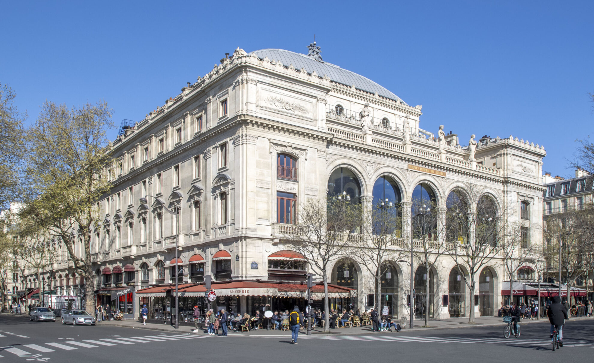 Façade du Théâtre du Châtelet avec ses grandes arches, ses sculptures et ses terrasses donnant sur une place parisienne.