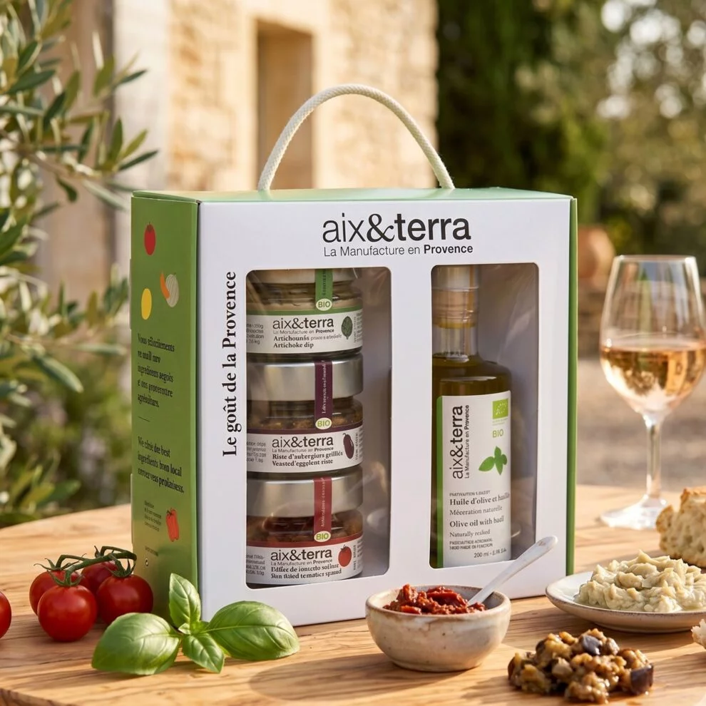 Coffret apéritif bio Aix&Terra avec trois tartinables provençaux et une bouteille d'huile d'olive au basilic, présenté sur une table en bois avec tomates, basilic et un verre de vin.