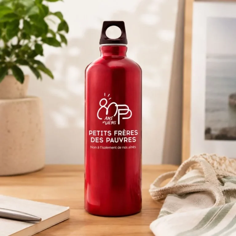 Gourde en aluminium rouge floquée du logo « 80 ans » et du texte « Petits Frères des Pauvres, non à l'isolement de nos aînés », posée sur un bureau en bois.