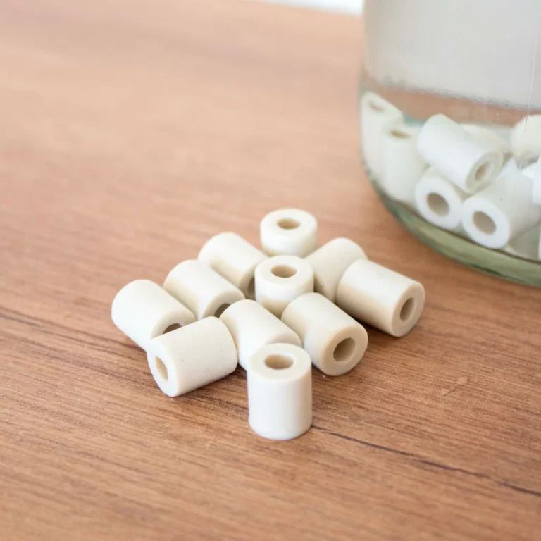 Perles de céramique blanches cylindriques posées sur une table en bois, à côté d'un bocal en verre rempli d'eau contenant d'autres perles.